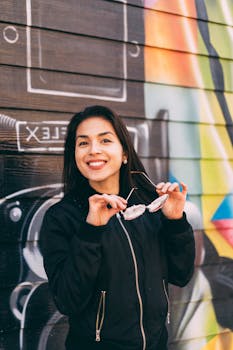 一位快乐的女士戴着太阳镜，在户外彩色涂鸦墙前摆姿势