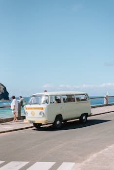 Classic yellow vintage van driving along the scenic seaside road on a sunny day.