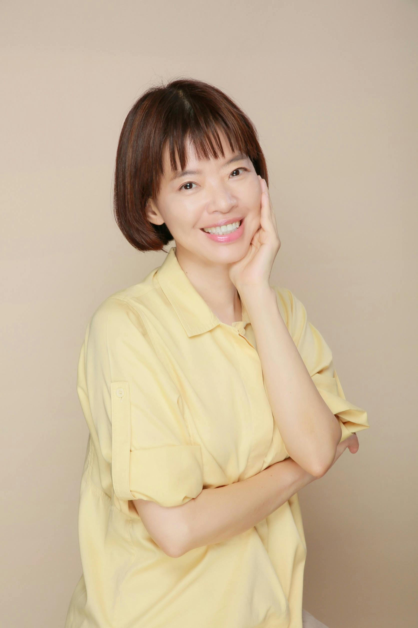 Cheerful woman in a yellow shirt posing in a studio setting, exuding happiness.