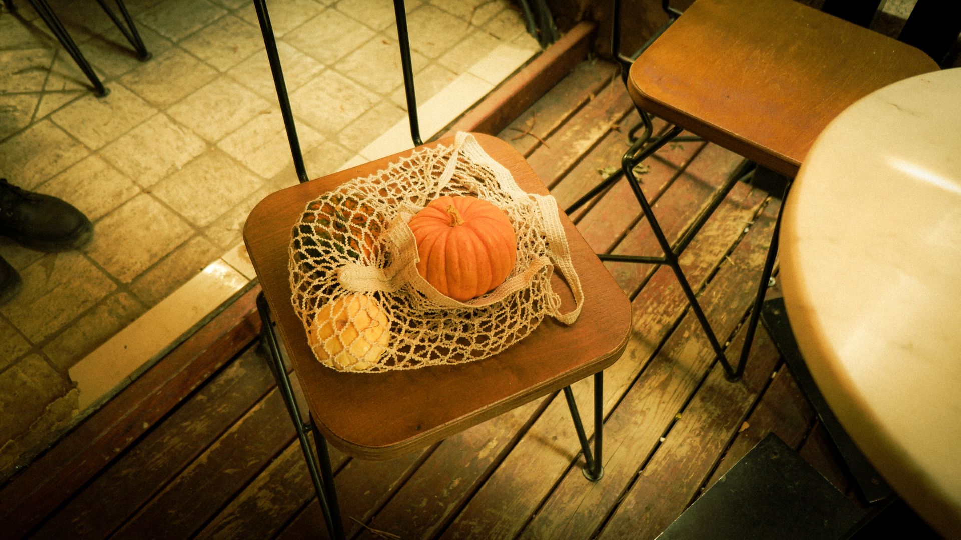 A cozy autumn scene with pumpkins in a mesh bag on a wooden chair indoors.