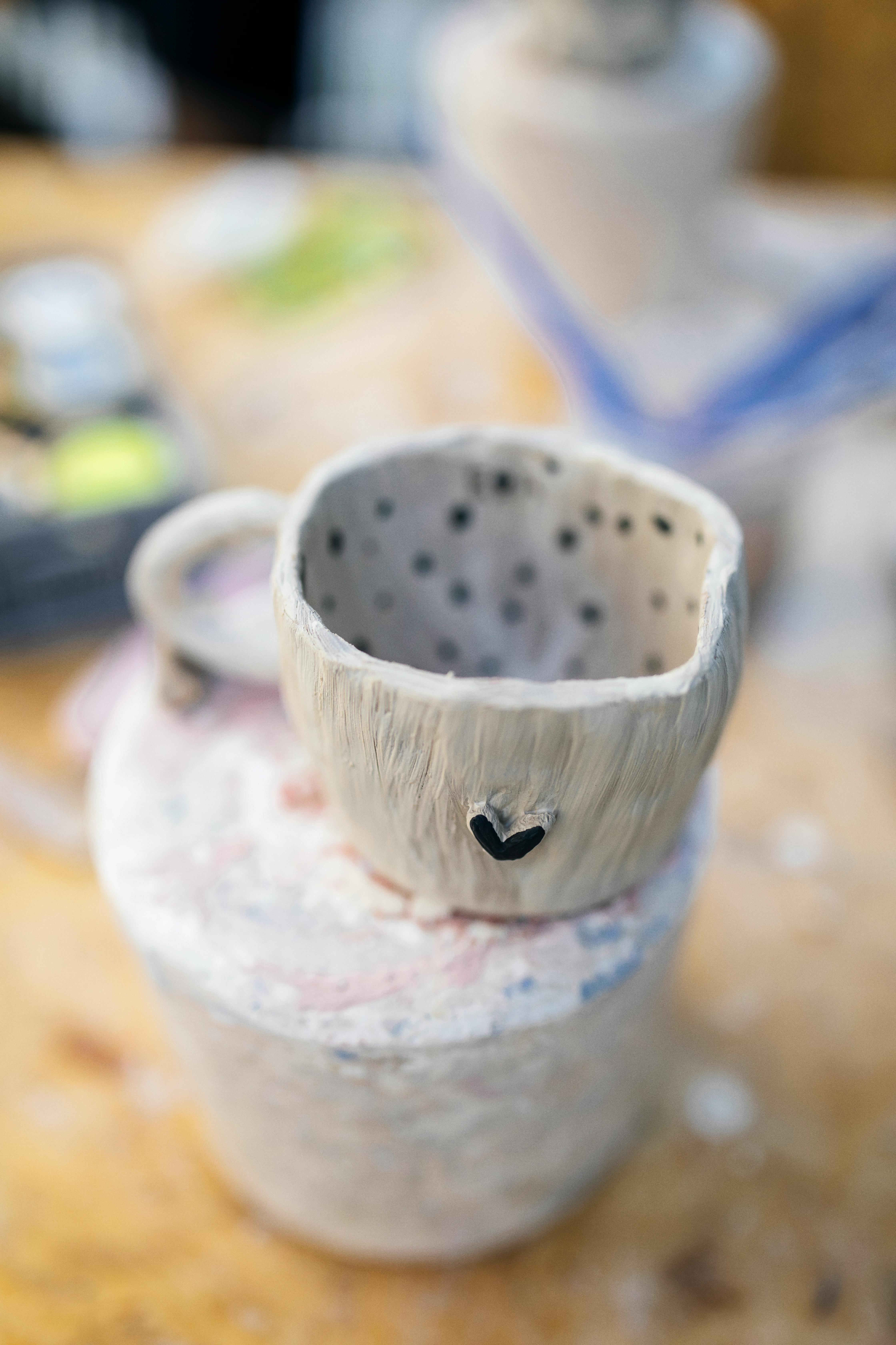 A unique handmade pottery mug with a rustic heart design on a wooden table.