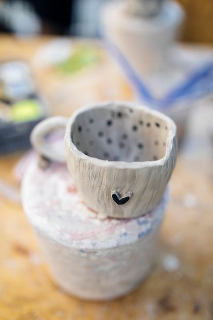 A unique handmade pottery mug with a rustic heart design on a wooden table.