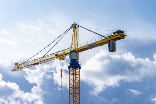 Free A towering yellow crane extends into a bright blue sky dotted with fluffy clouds. Stock Photo