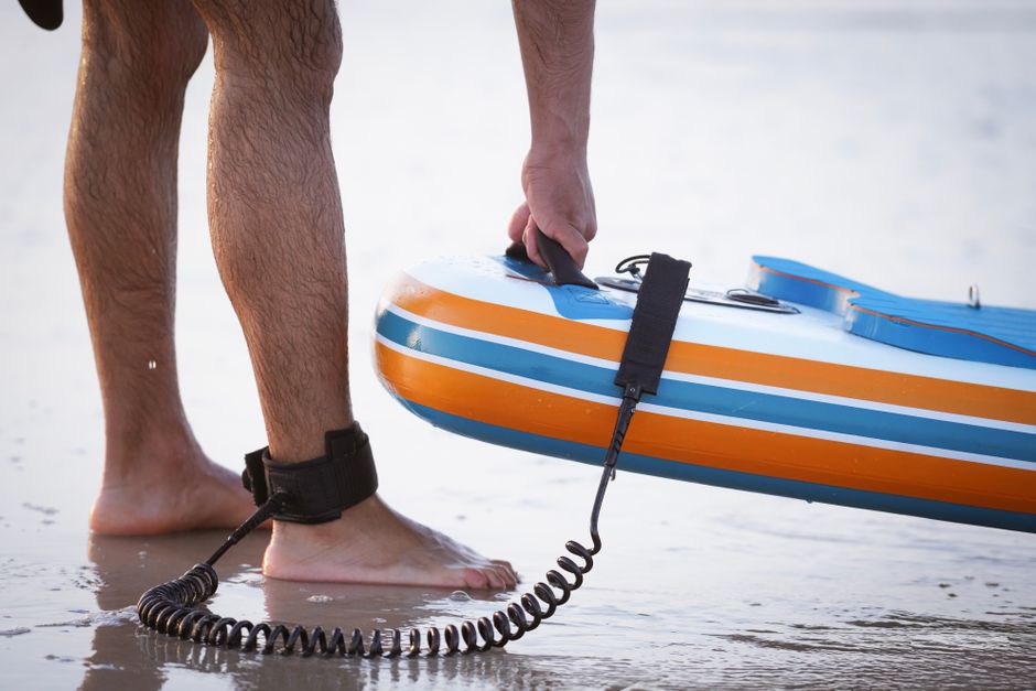 Close-up of a man holding a paddleboard while standing on the beach sand.