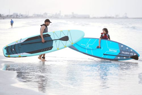 Free Man and child with surfboards walking along the beach shore, enjoying water sports. Stock Photo