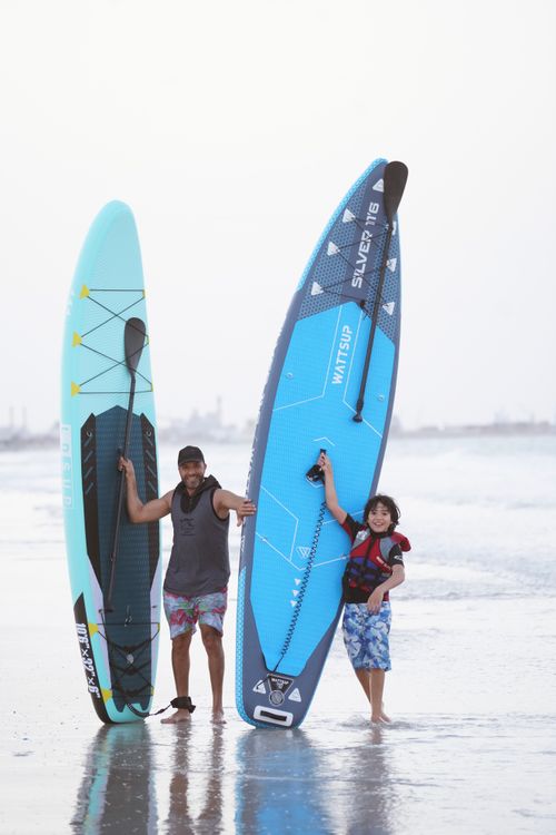 Free Father and son holding paddleboards at the beach, ready for a surfing adventure on a sunny day. Stock Photo