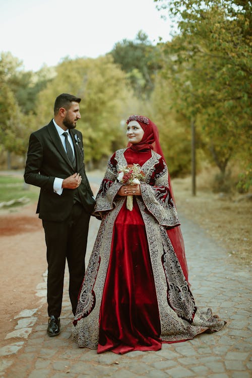 Groom in a Tuxedo and the Bride in a Traditional Red Wedding Dress on the Walkway in the Park