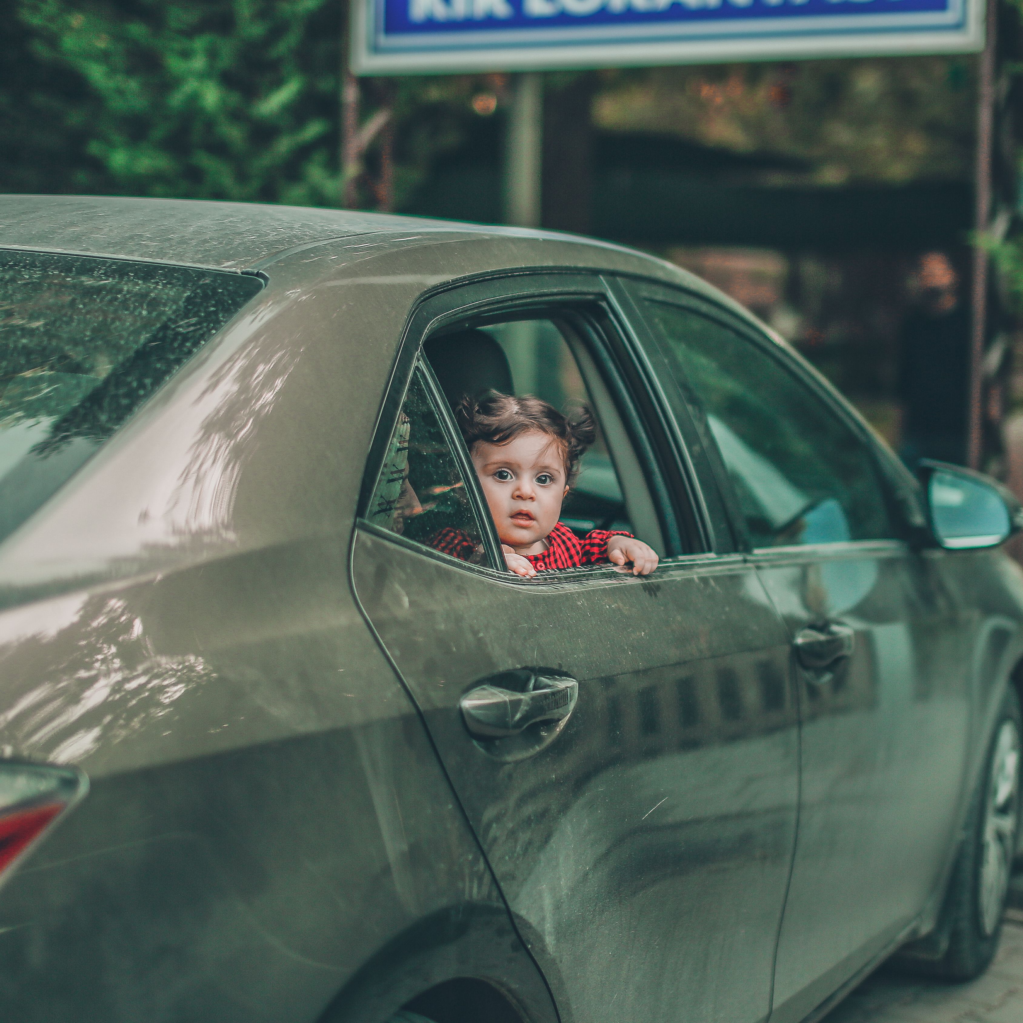 A child with curly brown hair peeks out from a car window, portraying curiosity and playfulness.