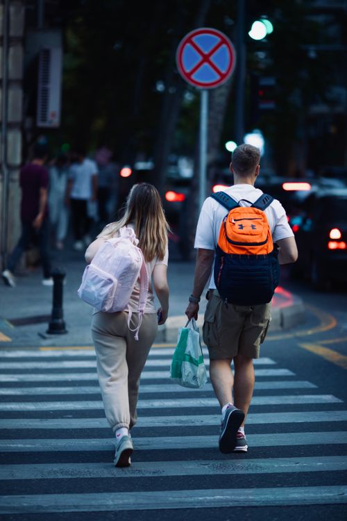 Free A couple crosses a busy urban street in Baku, Azerbaijan, carrying backpacks under city lights. Stock Photo