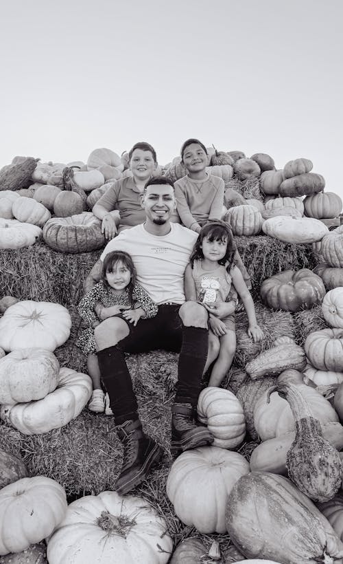 Man with a Group of Children Sitting on a Pile of Hay and Pumpkins 