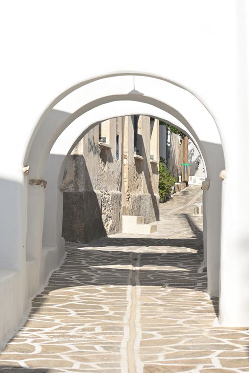 Free Scenic view of a traditional stone alleyway under a white arch in Pyrgos, Greece, capturing the essence of Greek island architecture. Stock Photo