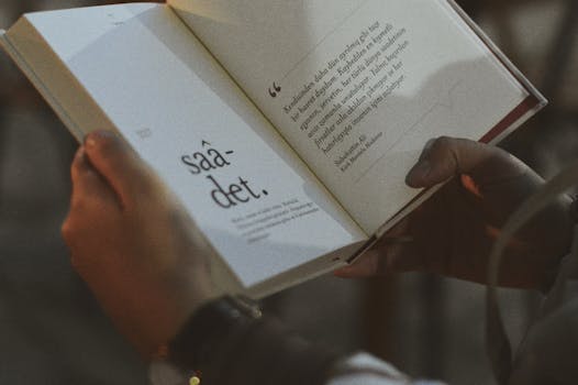 Person holding and reading an open book with visible text.