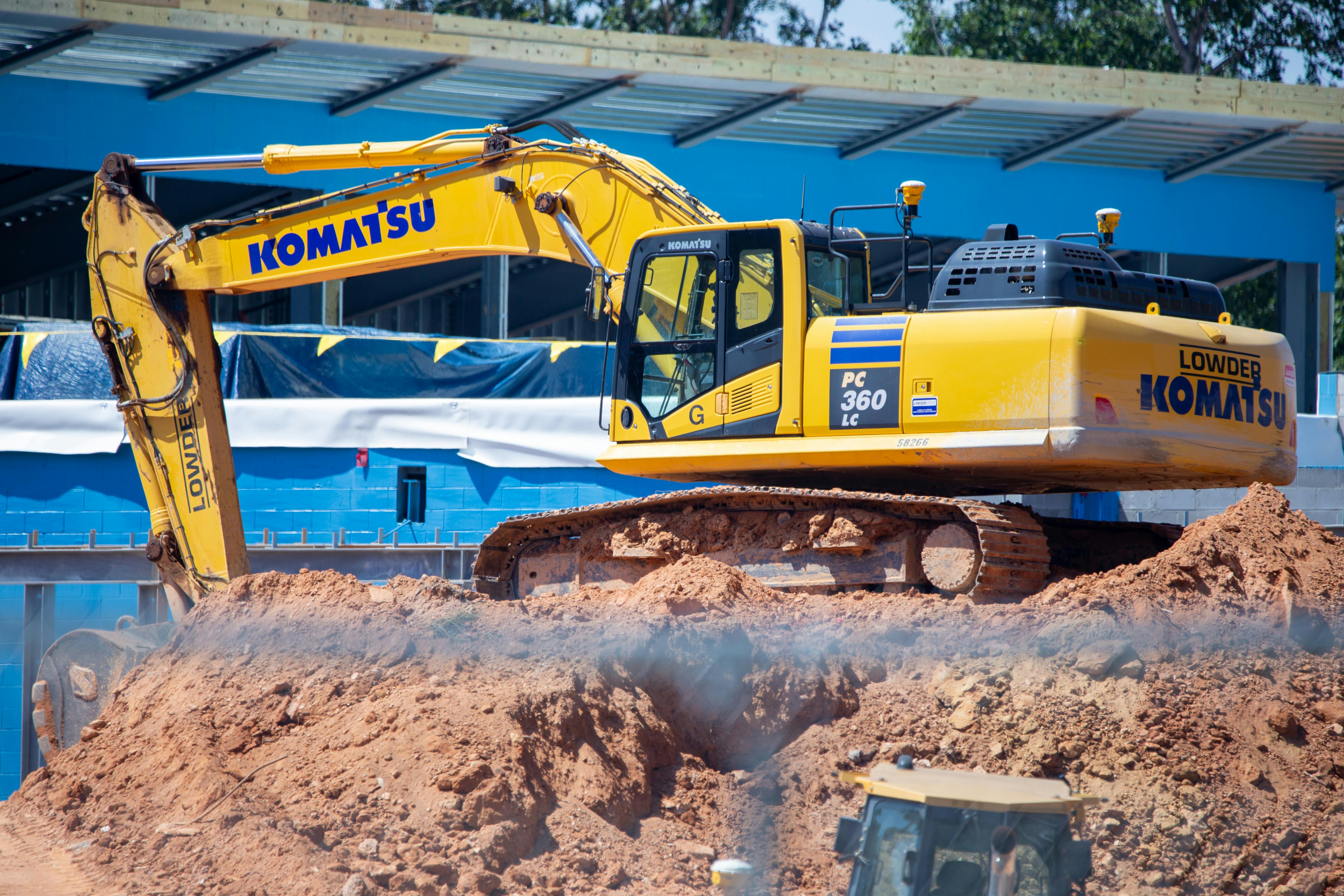 A bright yellow Komatsu excavator working on a construction site, moving piled earth.