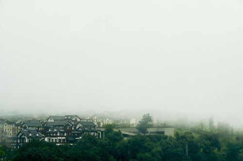 Free Serene landscape of a town shrouded in dense fog with lush greenery. Stock Photo