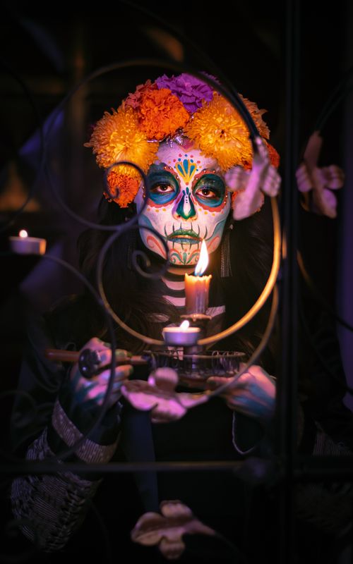 Free A dramatic portrait of a Catrina face-paint with vibrant flowers and candlelight. Stock Photo