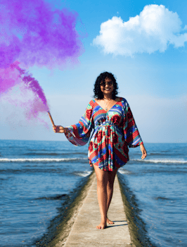 夏天，一个快乐的女人在海边的石码头上拿着紫色烟雾弹