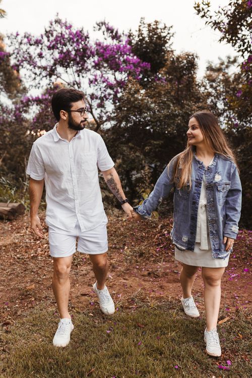 Free Young couple in casual outfits holding hands and walking outdoors surrounded by flowers. Stock Photo