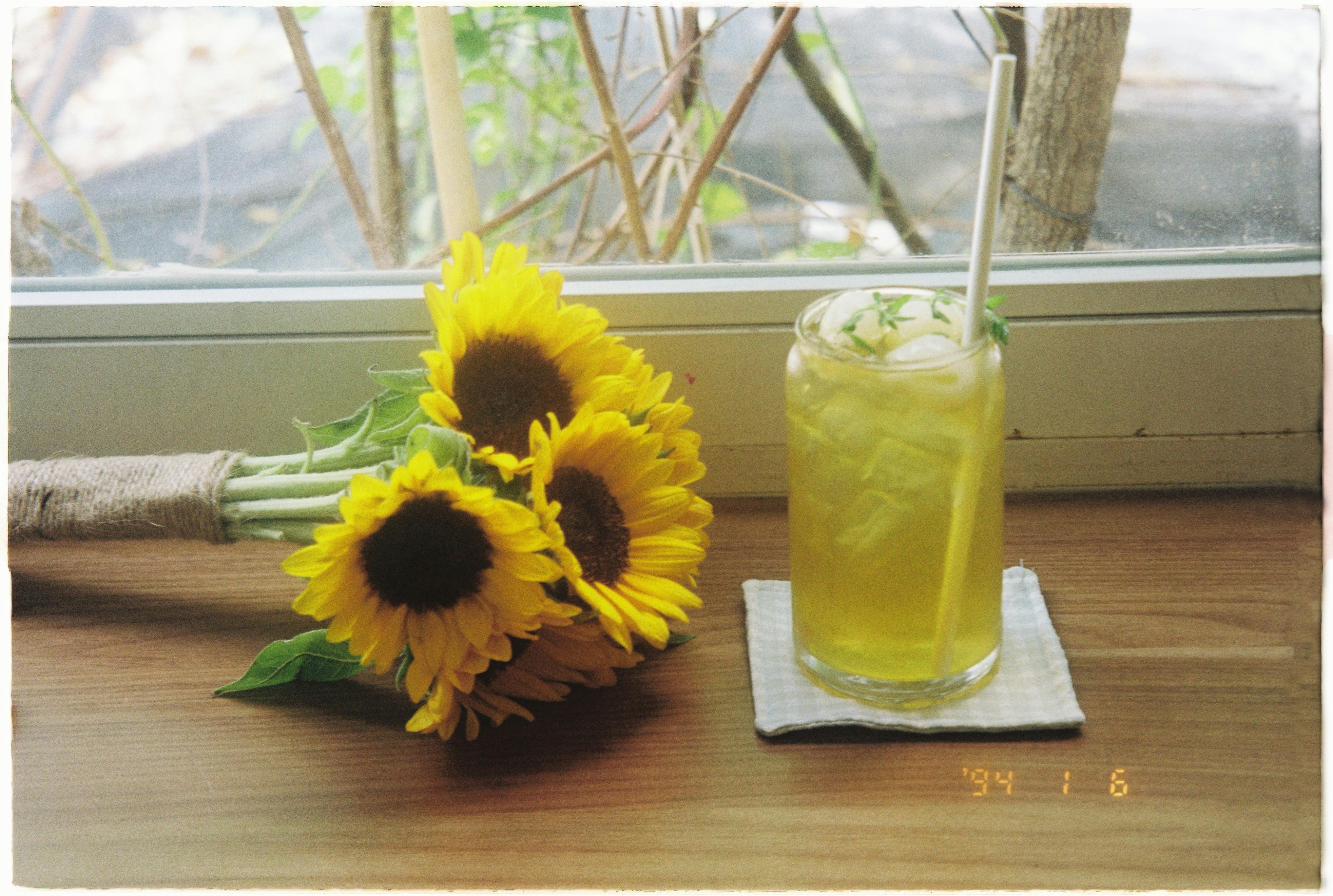 A close-up of a refreshing iced drink and a bouquet of sunflowers by a window.