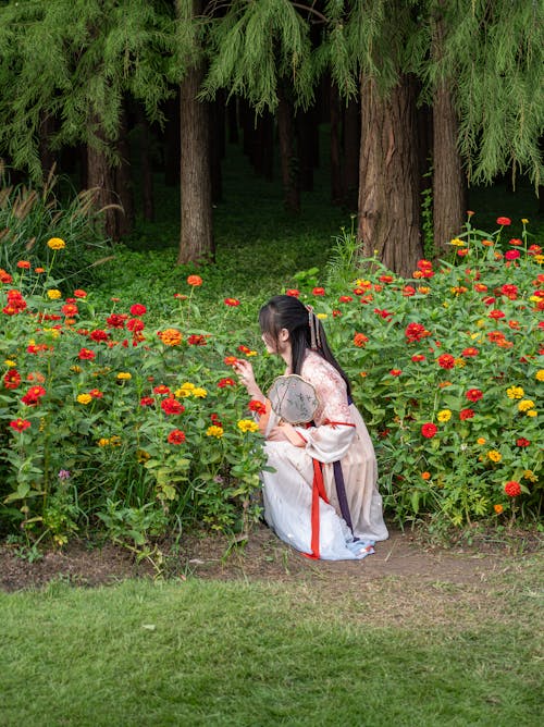 Woman in Traditional Clothing Squatting by Colorful Flowers