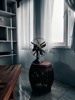 A vintage fan surrounded by soft curtains in a sunlit Indian room corner, setting a serene mood.