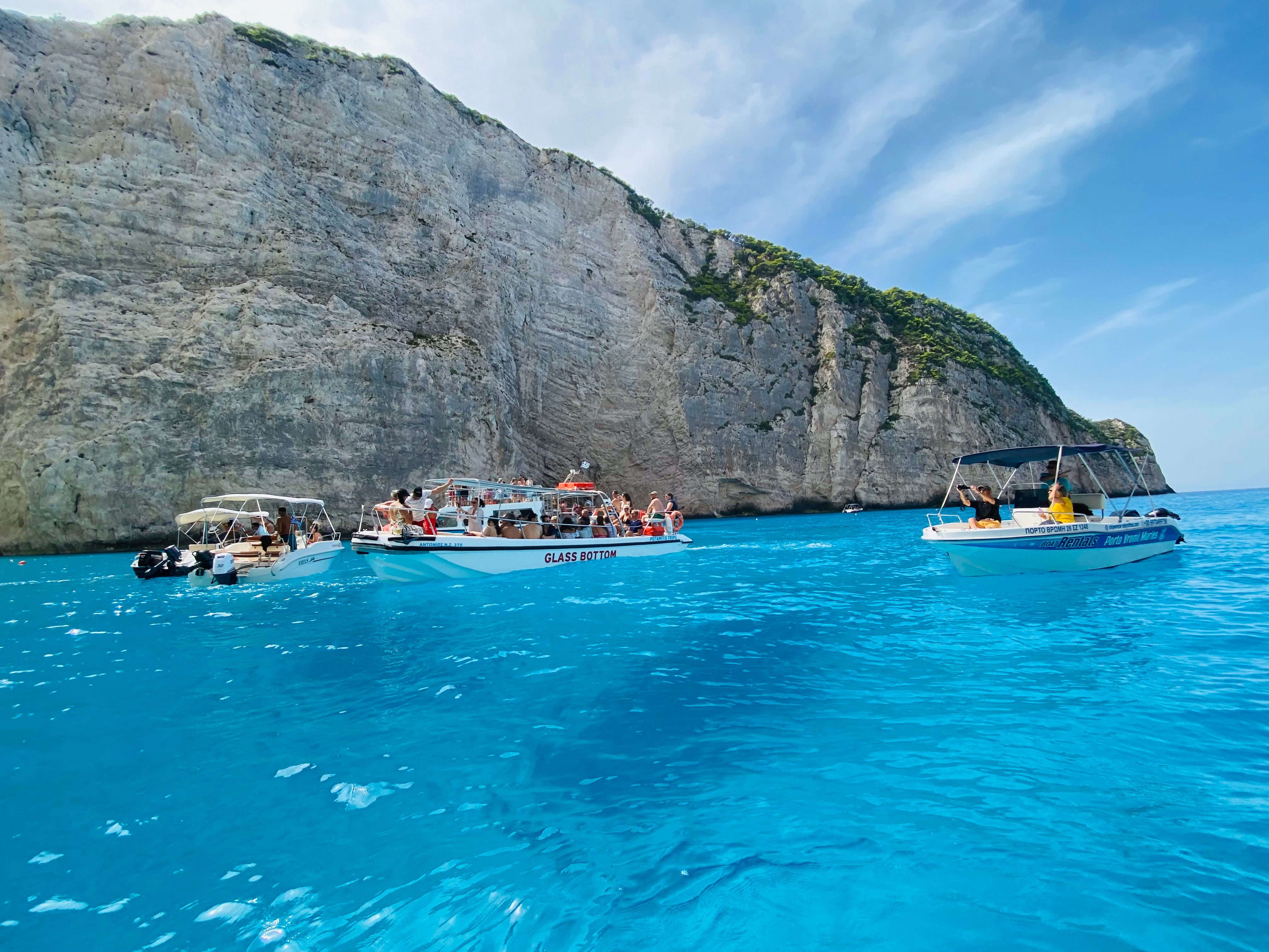 Tour boats in vibrant turquoise waters near a stunning limestone cliff under clear skies.