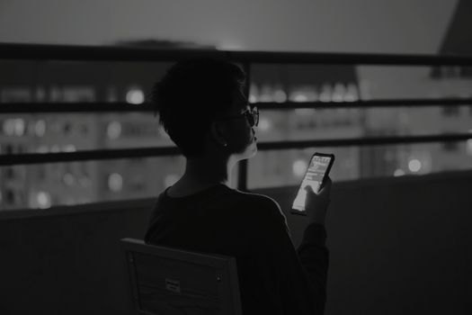 Silhouette of a person texting on a balcony at night, with city lights in the background.