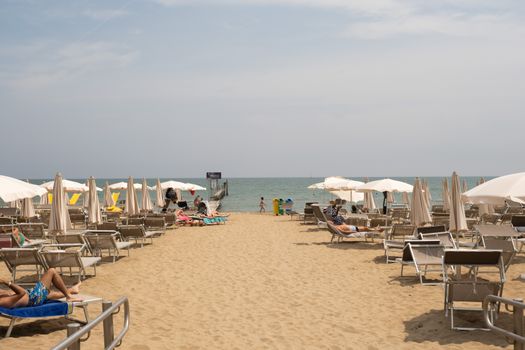 Tourists enjoying a sunny day at Lido di Jesolo beach in Veneto, Italy, with sun loungers and umbrellas.