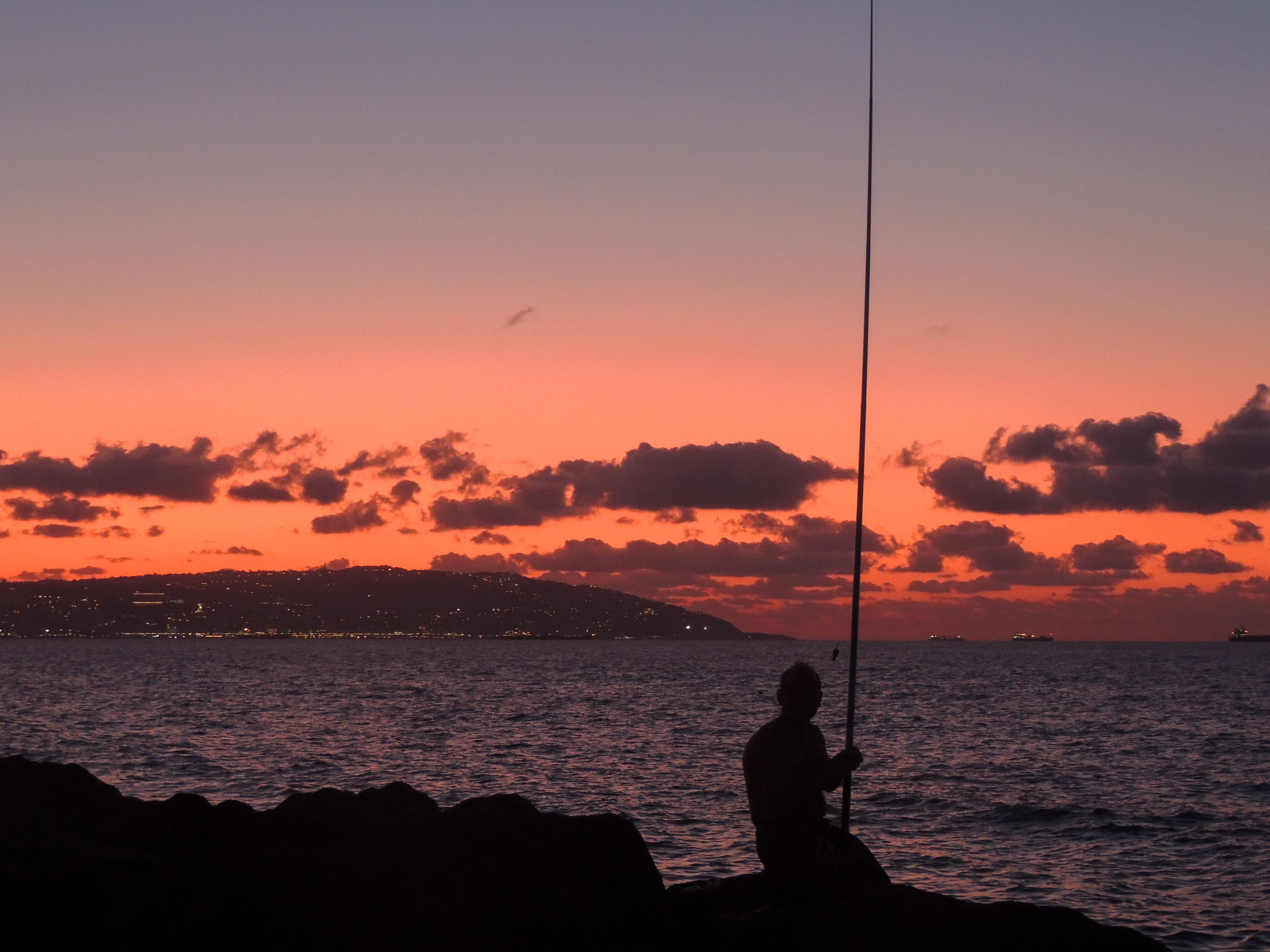 Man Sits with Fishing Road by Ocean at Sunset · Free Stock Photo