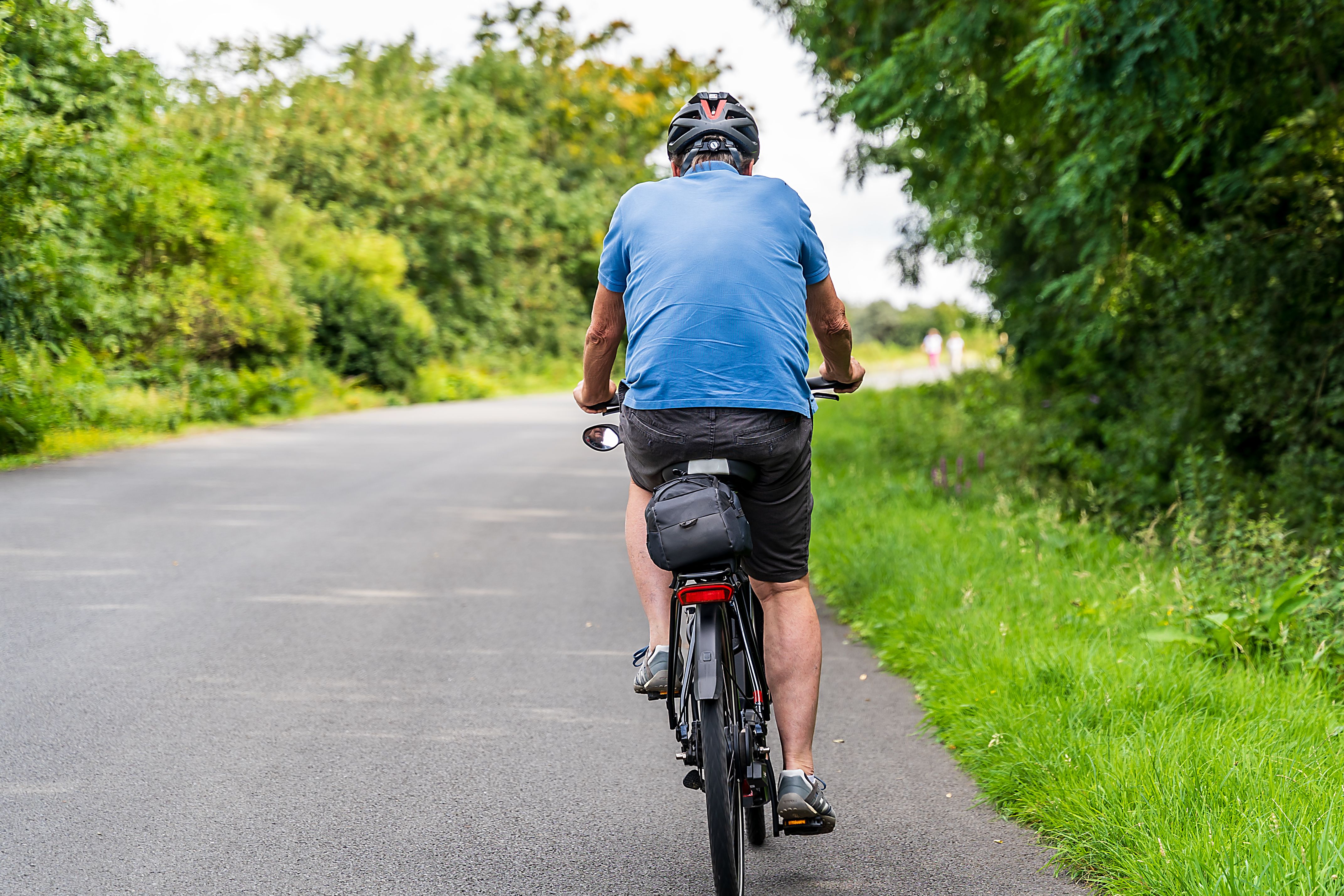 Elderly man biking on a rural road, enjoying an outdoor exercise ride.