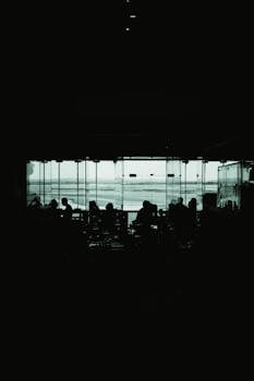 Silhouetted people in an airport lounge against large windows overlooking the runway.