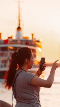 Woman capturing a sunset by the sea in İstanbul using her smartphone.