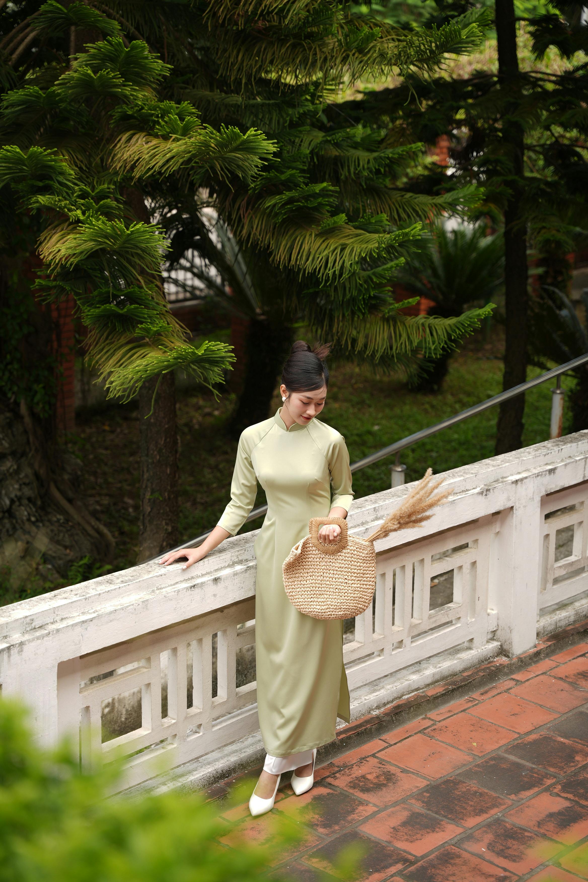 Serene woman in a green dress holding a bag, enjoying nature.