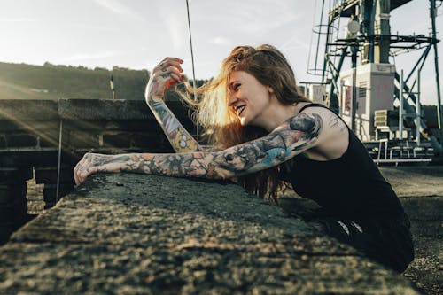 Smiling Woman with Tattoos Leaning on Wall