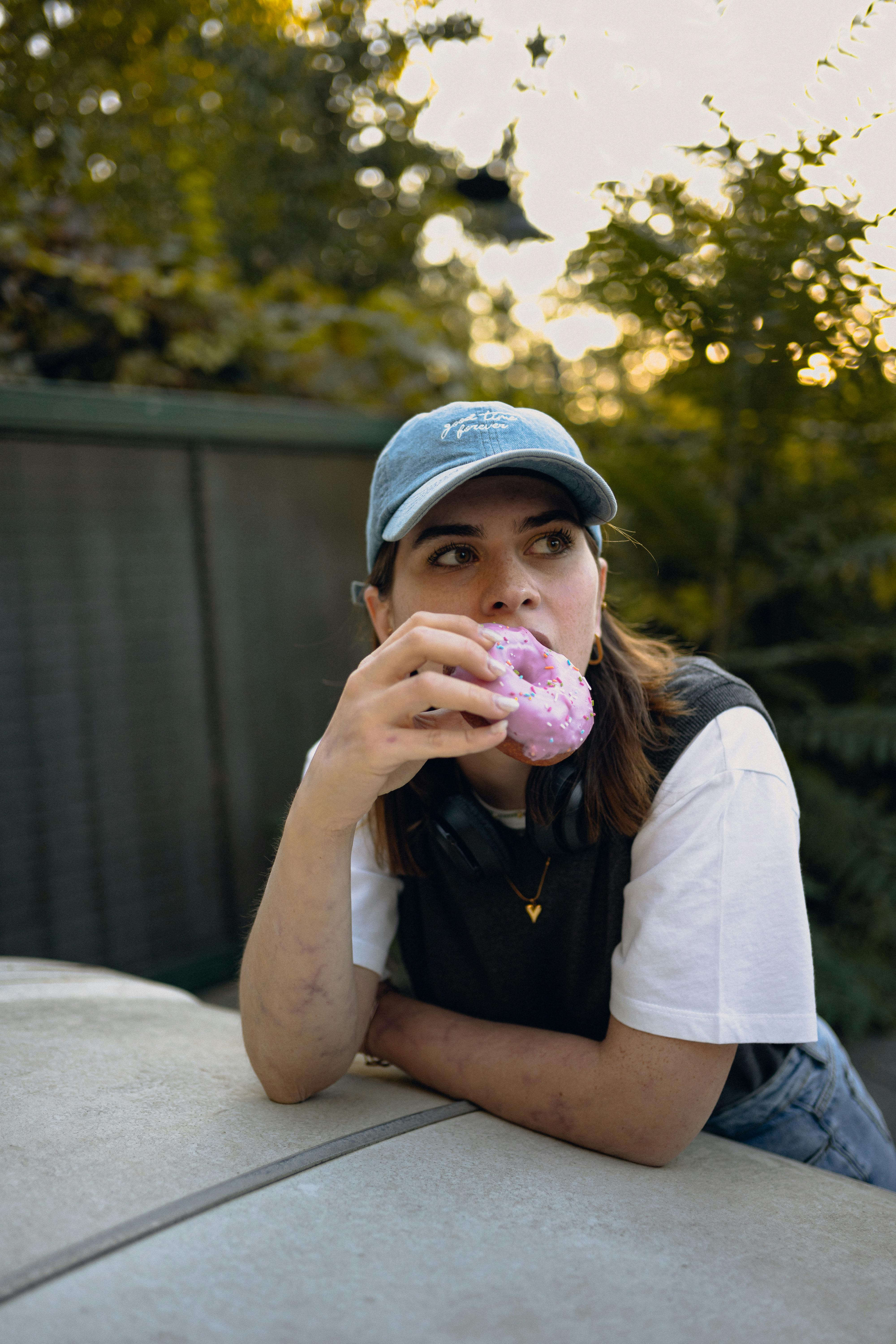 Woman in Cap and Vest Sitting by Car and Eating Sweet Donut · Free ...
