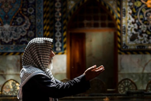 Elderly man in Karbala mosque, praying with hands raised, wearing a keffiyeh.