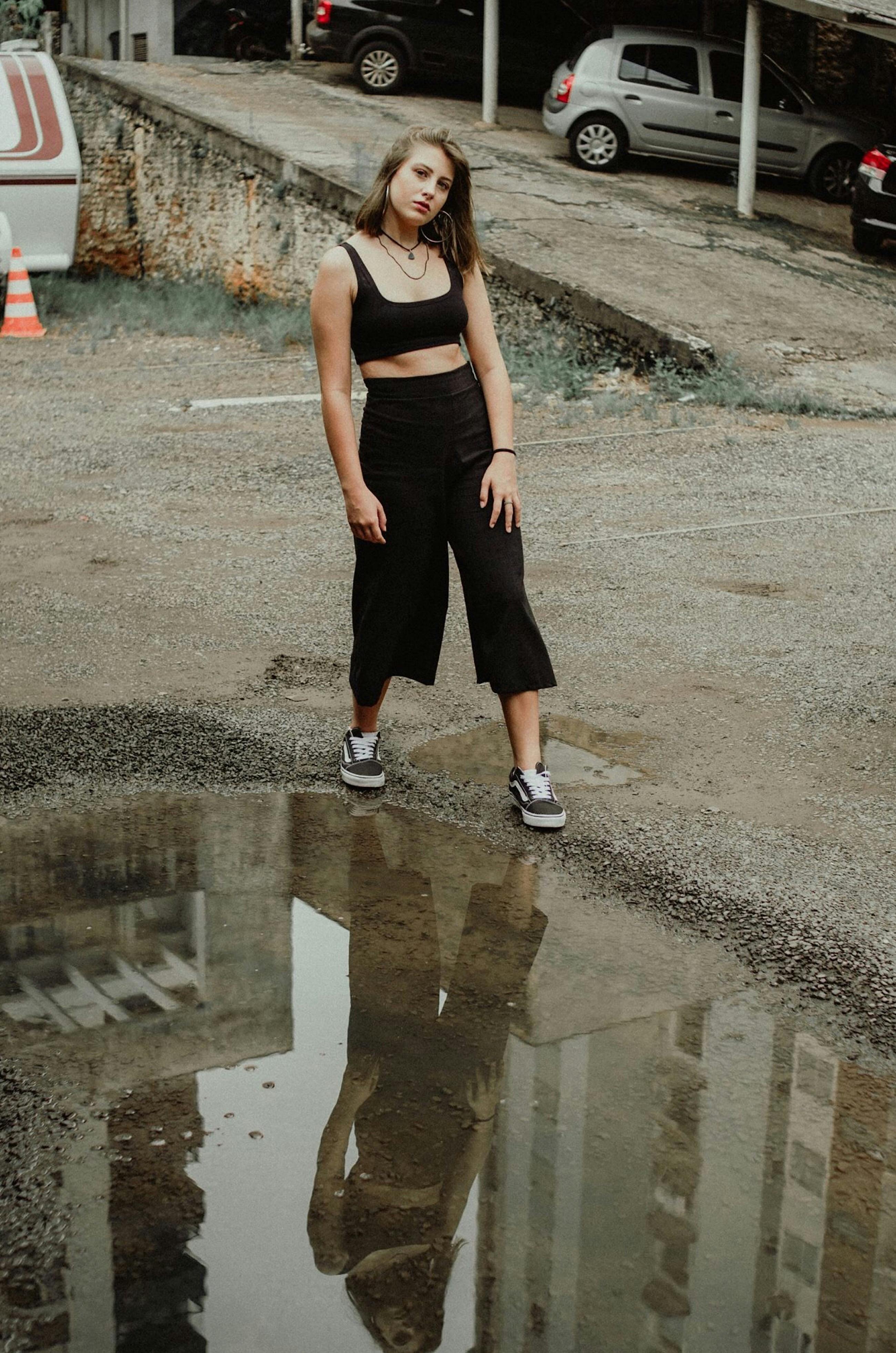 Fashion-forward woman posing in urban setting with puddle reflection.
