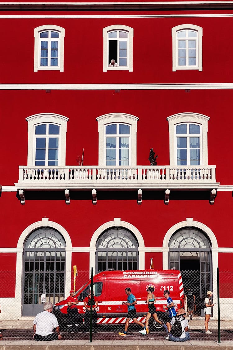 People Running By Red Building Wall