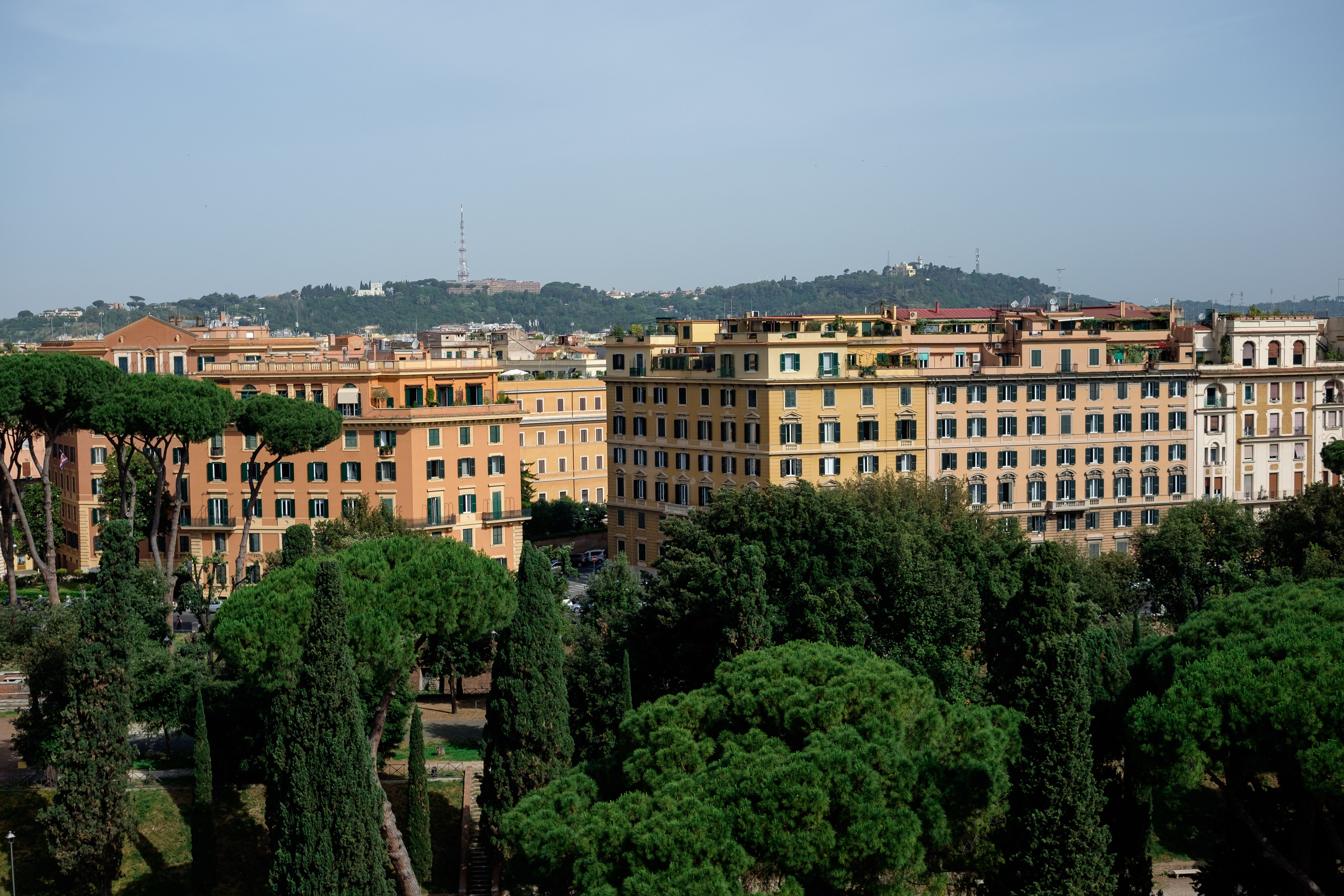 An aerial view of Rome with classic architecture surrounded by lush greenery on a clear day.