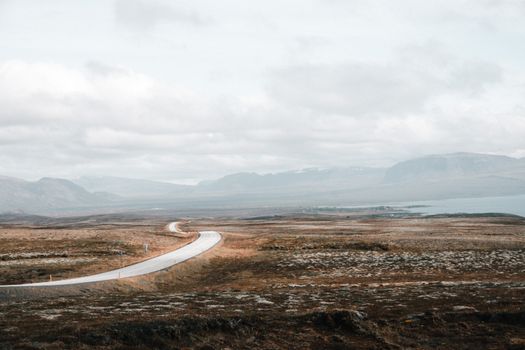 A winding road cutting through a barren and expansive countryside landscape under an overcast sky.