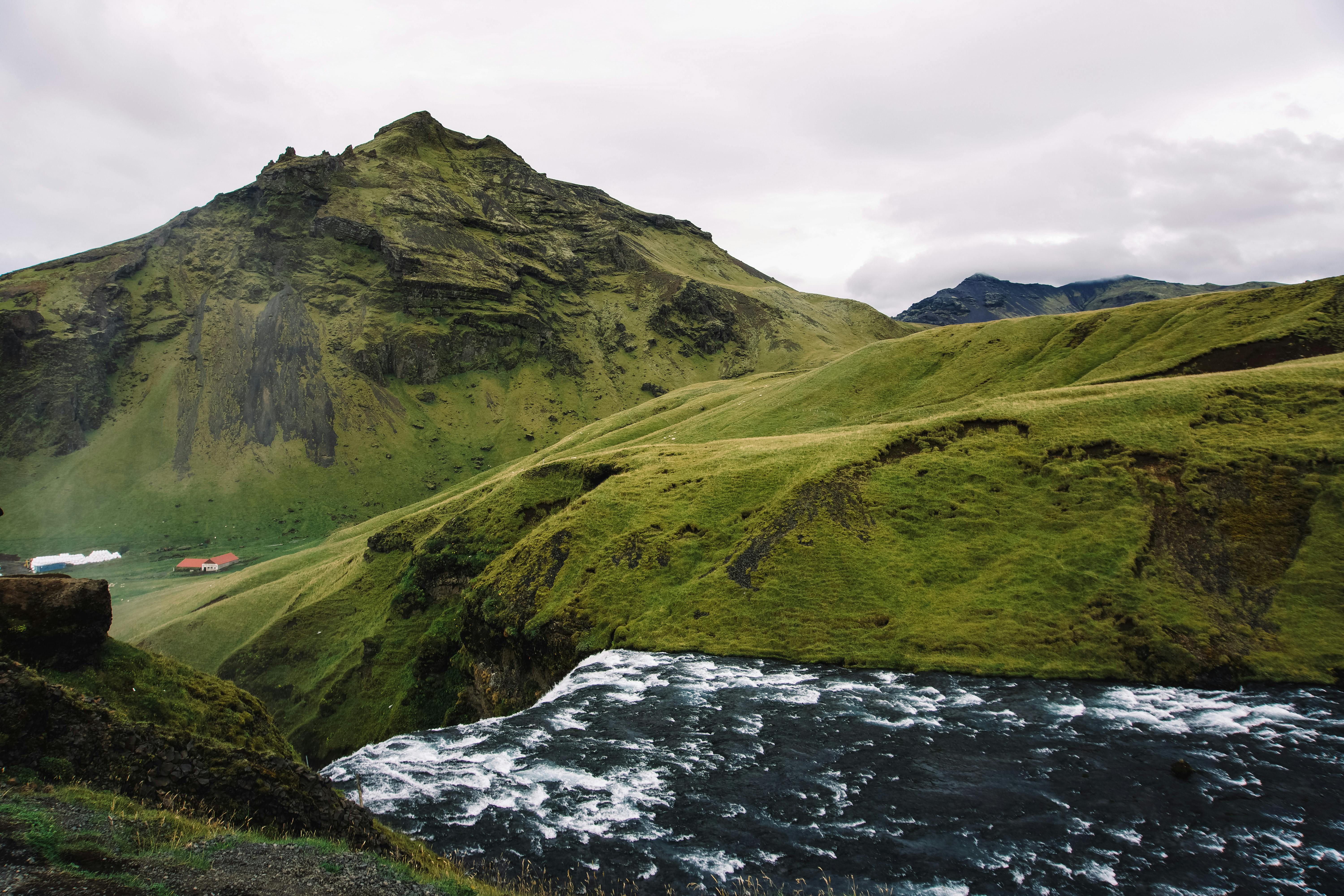 Breathtaking aerial view of a waterfall cascading down lush green hills in Iceland. Ideal for nature lovers.