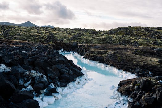 Aerial view of a rugged volcanic landscape with a bright blue geothermal stream amidst rocky terrain.