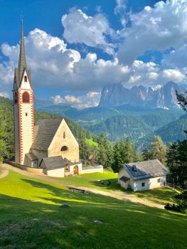 Picturesque view of a church in Ortisei village, surrounded by Dolomite mountains and lush forests.