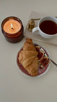 Cozy breakfast scene with a croissant, figs, and tea by candlelight.