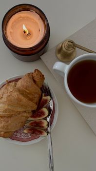 Warm breakfast setting featuring croissant, figs, tea, and a candle.