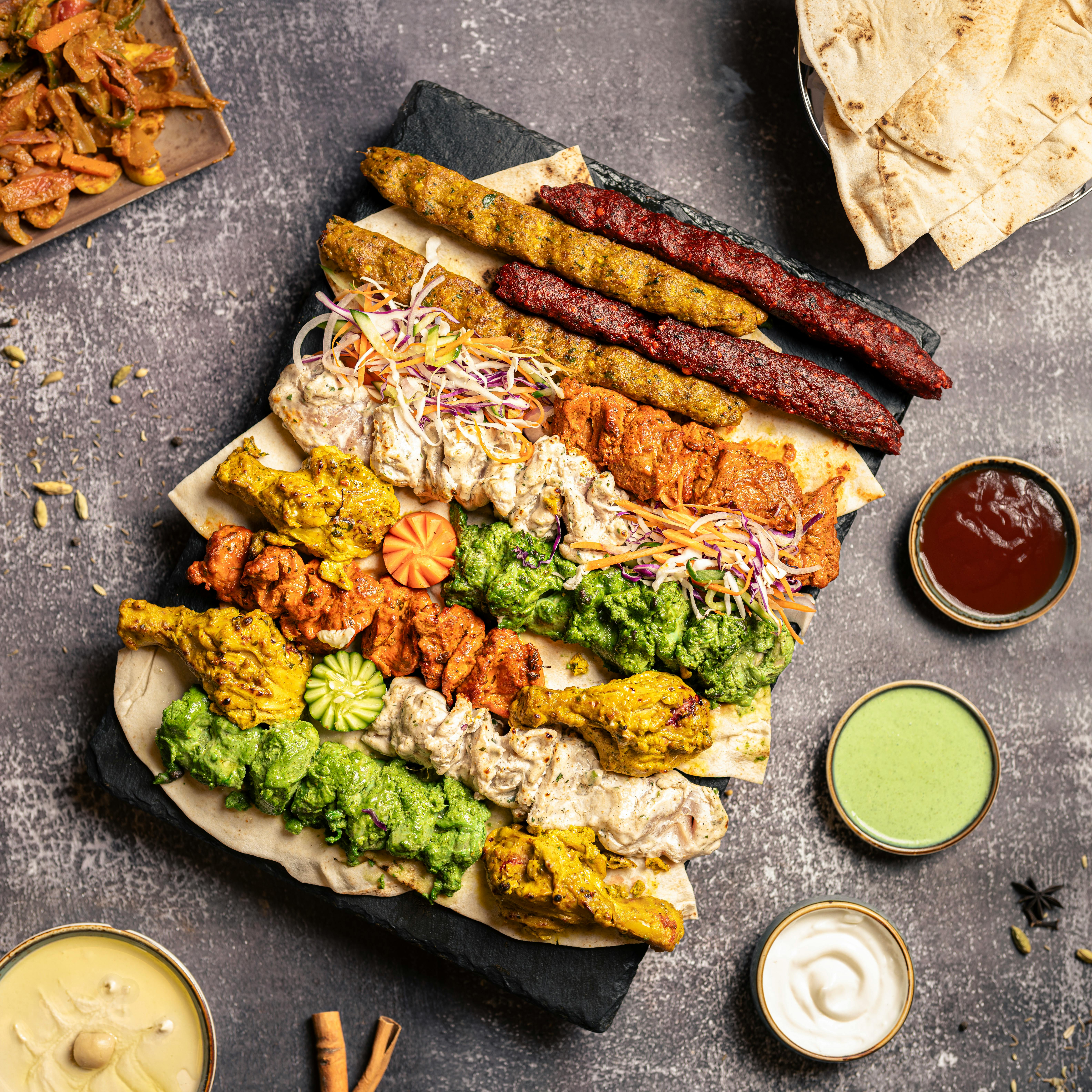 aboodi vesakaran - Savory Middle Eastern grilled meat platter with vibrant sauces and fresh vegetables.