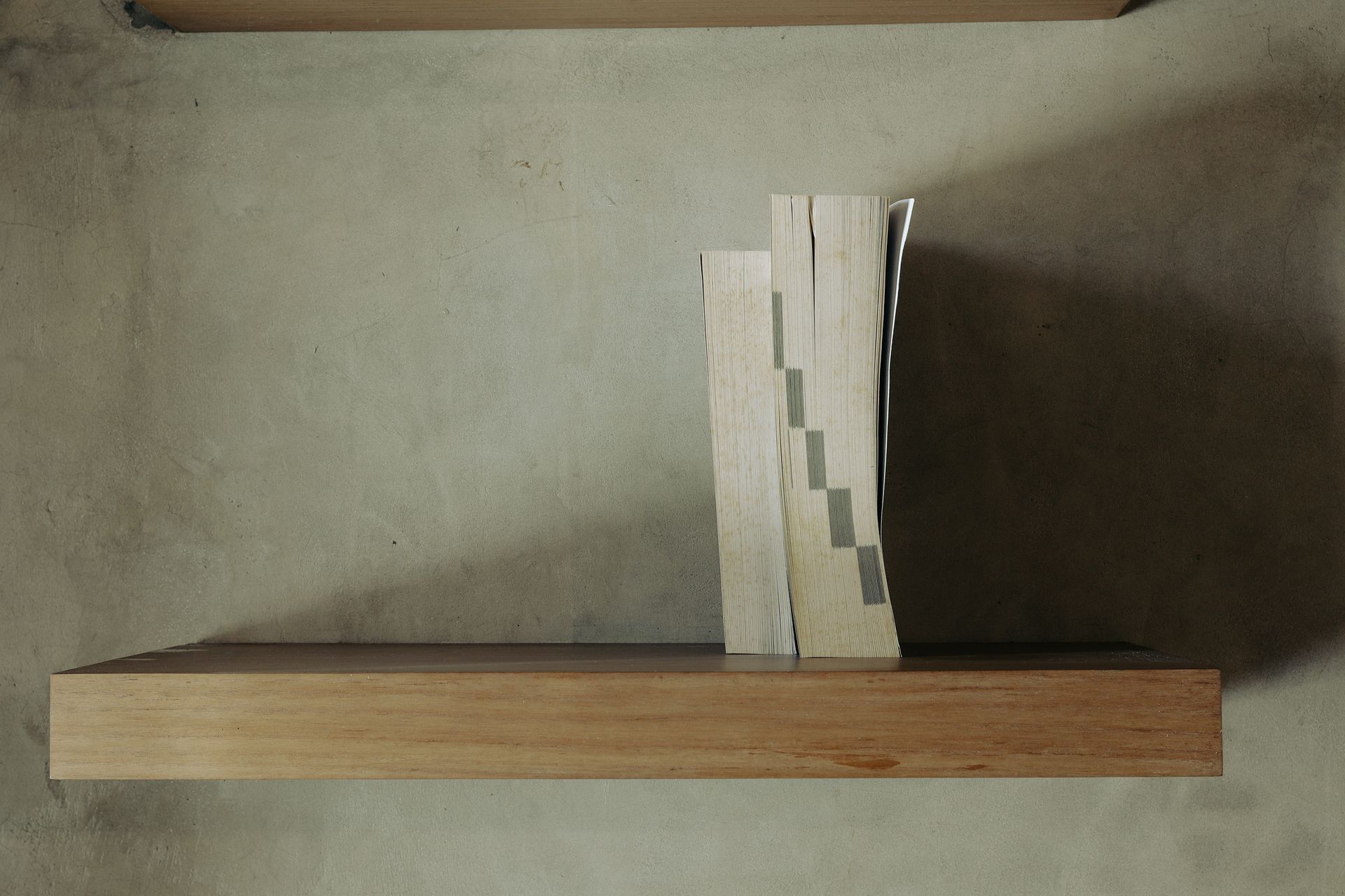 Artistic minimalist photo of books on a wooden shelf against a concrete wall.