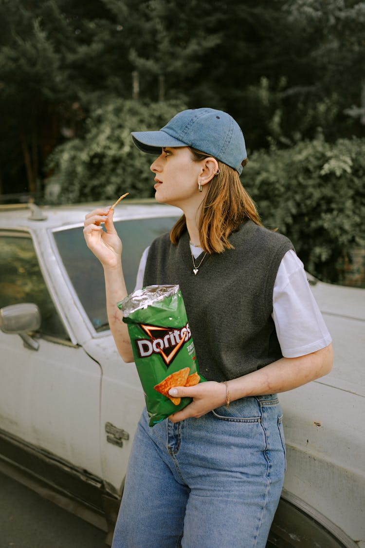 Woman In Cap Eating Doritos By Car