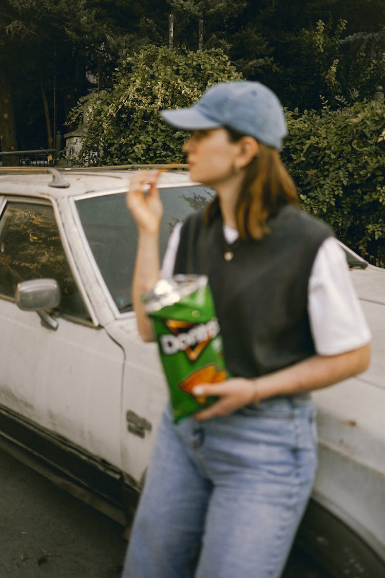 Woman Standing Beside A Car And Eating Crisps