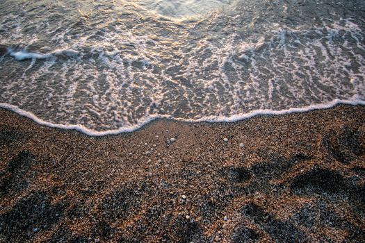 A peaceful beach scene showcasing waves gently lapping on a pebbled shore under soft lighting.