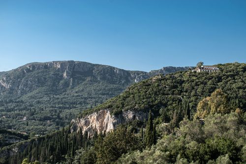 Free A picturesque Mediterranean landscape featuring lush greenery and mountains with a hilltop villa. Stock Photo